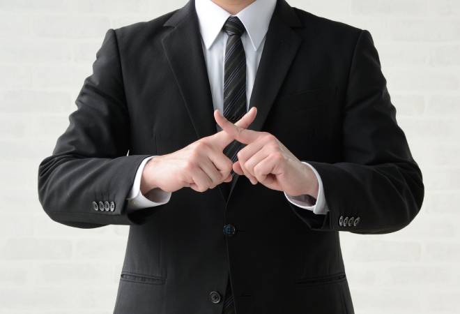 スーツの男性が指で×印を作っている。